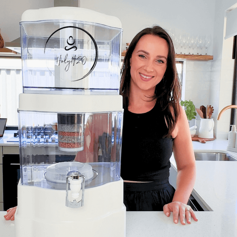 Person standing next to the HolyH₂O™ Trinity Filter in a modern kitchen, showcasing the water filtration system.